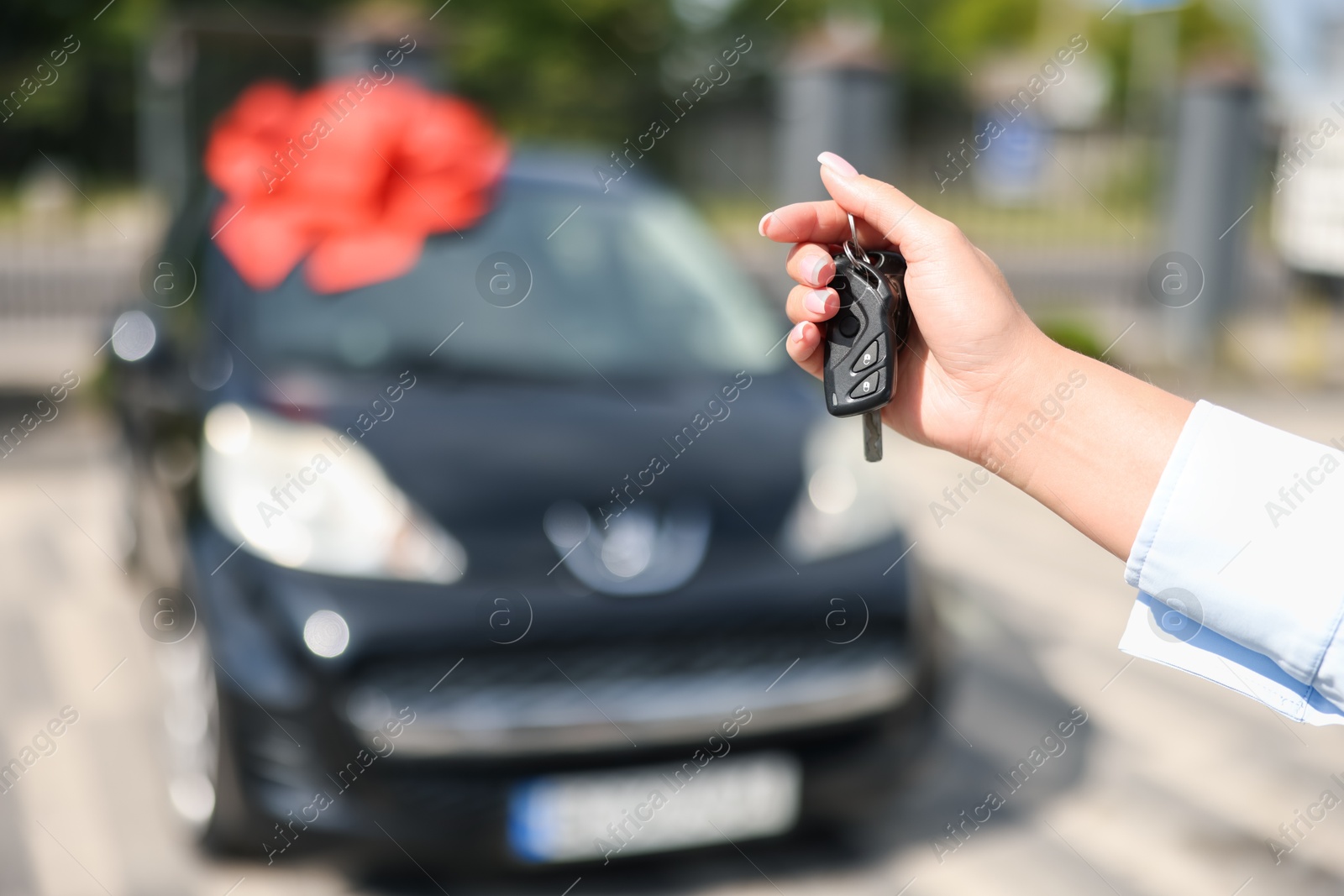 Dreams come true. Woman holding car key near her new auto with big red bow outdoors, closeup Photo of Dreams come true. Woman holding car key near her new auto with big red bow outdoors, closeup