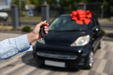 Photo of Dreams come true. Woman holding car key near her new auto with big red bow outdoors, closeup