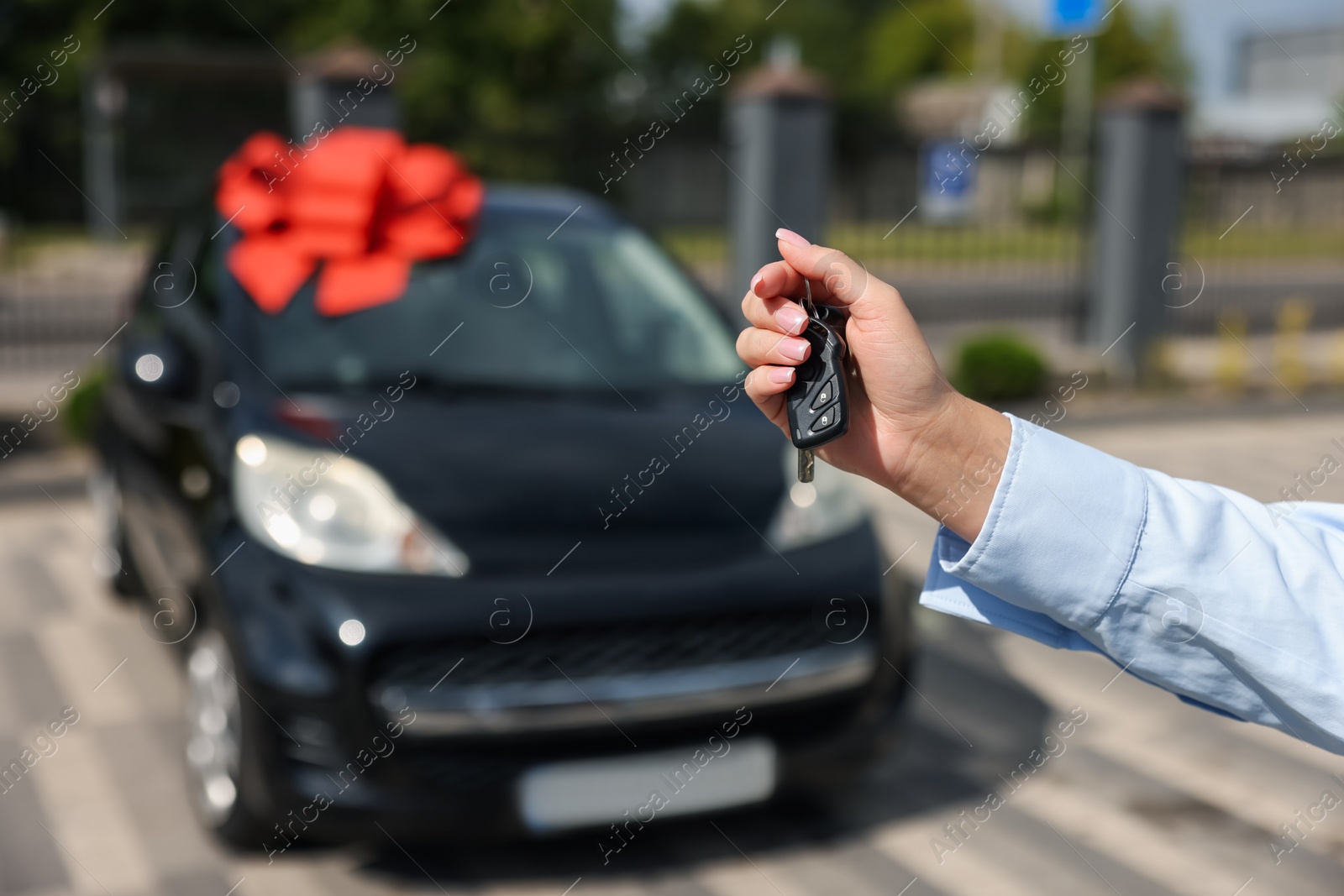 Dreams come true. Woman holding car key near her new auto with big red bow outdoors, closeup Photo of Dreams come true. Woman holding car key near her new auto with big red bow outdoors, closeup