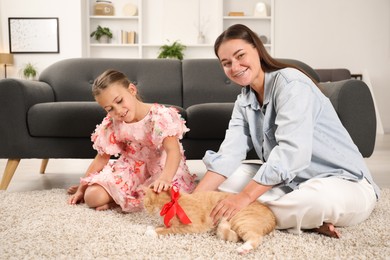 Photo of Dreams come true. Mother giving ginger cat with red bow to her daughter at home