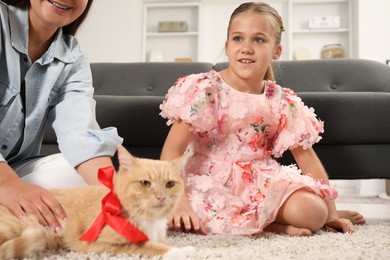 Photo of Dreams come true. Mother giving ginger cat with red bow to her daughter at home, closeup