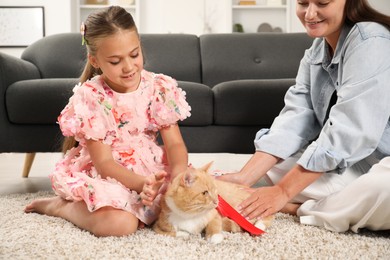 Photo of Dreams come true. Mother giving ginger cat with red bow to her daughter at home, closeup