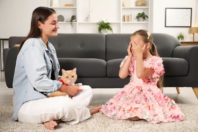 Photo of Dreams come true. Mother giving ginger cat with red bow to her daughter at home
