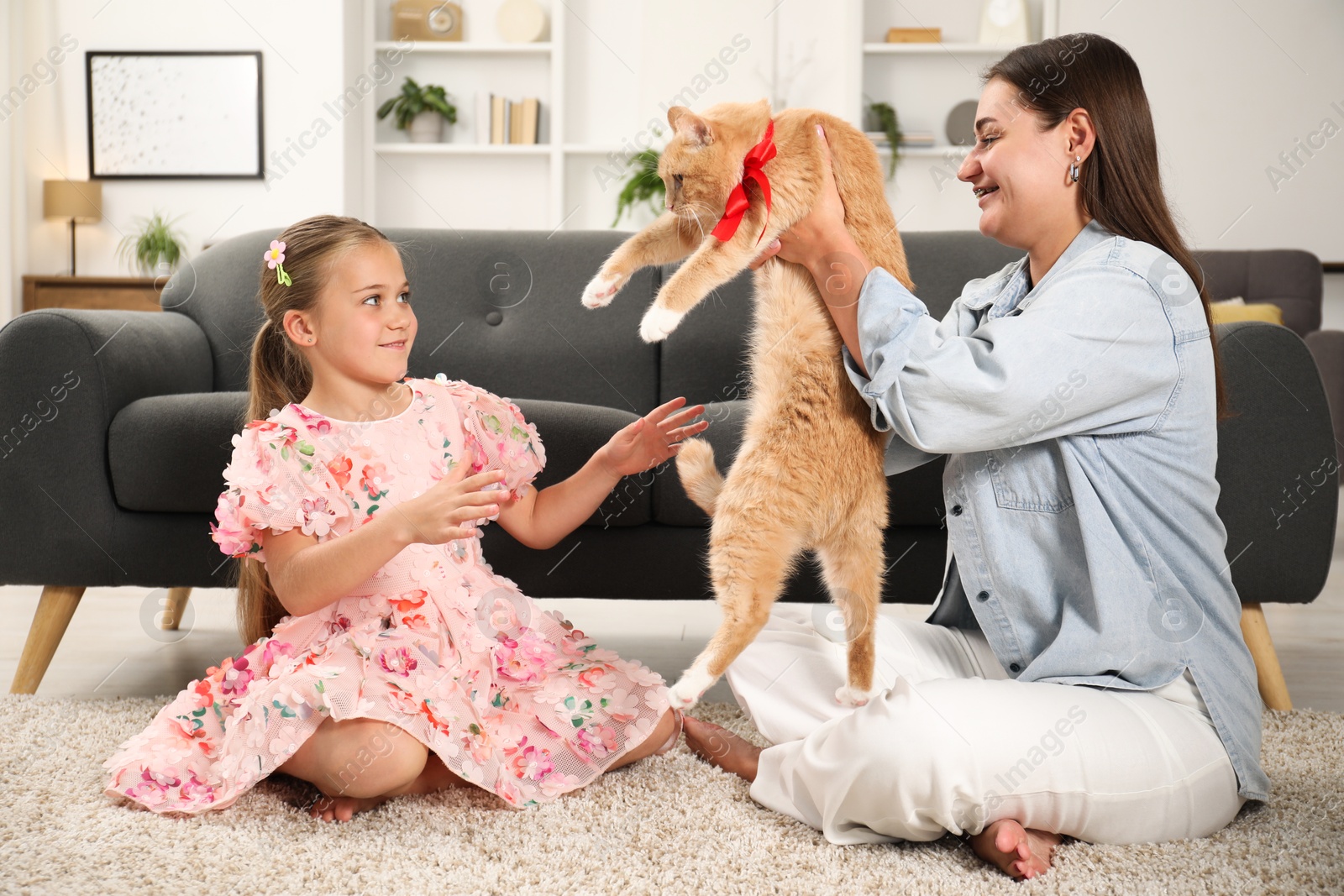 Photo of Dreams come true. Mother giving ginger cat with red bow to her daughter at home