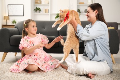 Photo of Dreams come true. Mother giving ginger cat with red bow to her daughter at home