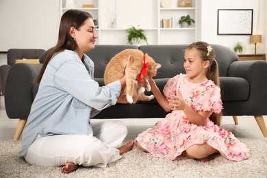 Photo of Dreams come true. Mother giving ginger cat with red bow to her daughter at home