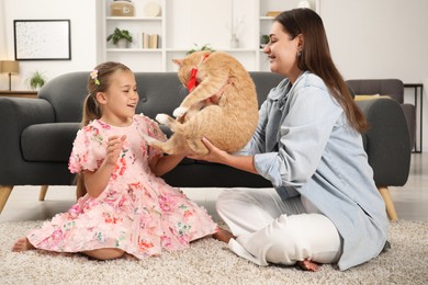 Photo of Dreams come true. Mother giving ginger cat with red bow to her daughter at home
