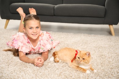 Photo of Dreams come true. Cute little girl stroking ginger cat with red bow on floor at home