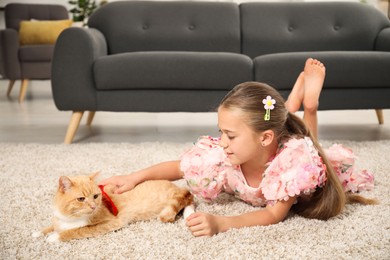 Photo of Dreams come true. Cute little girl stroking ginger cat with red bow on floor at home