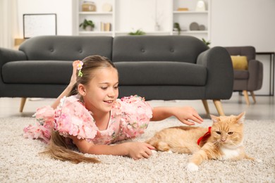 Photo of Dreams come true. Cute little girl stroking ginger cat with red bow on floor at home