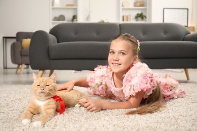 Photo of Dreams come true. Cute little girl stroking ginger cat with red bow on floor at home