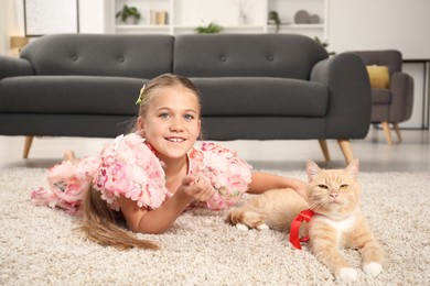 Photo of Dreams come true. Cute little girl stroking ginger cat with red bow on floor at home