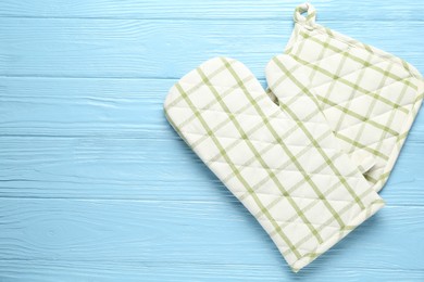 Photo of Oven glove and potholder on light blue wooden background, flat lay. Space for text