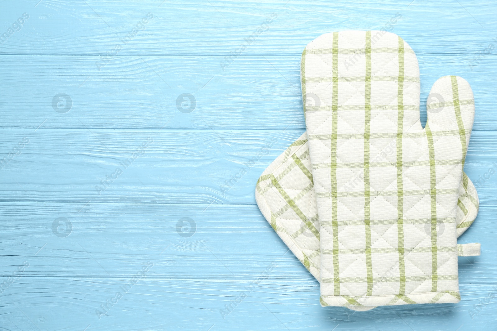 Photo of Oven glove and potholder on light blue wooden background, top view. Space for text