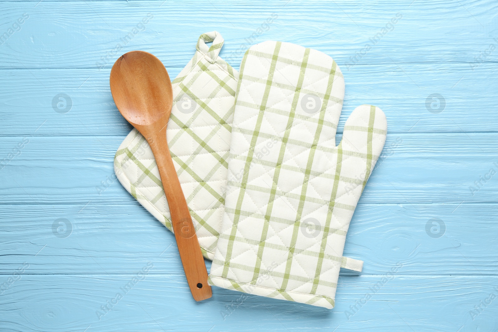 Oven glove, potholder and spoon on light blue wooden background, flat lay Photo of Oven glove, potholder and spoon on light blue wooden background, flat lay