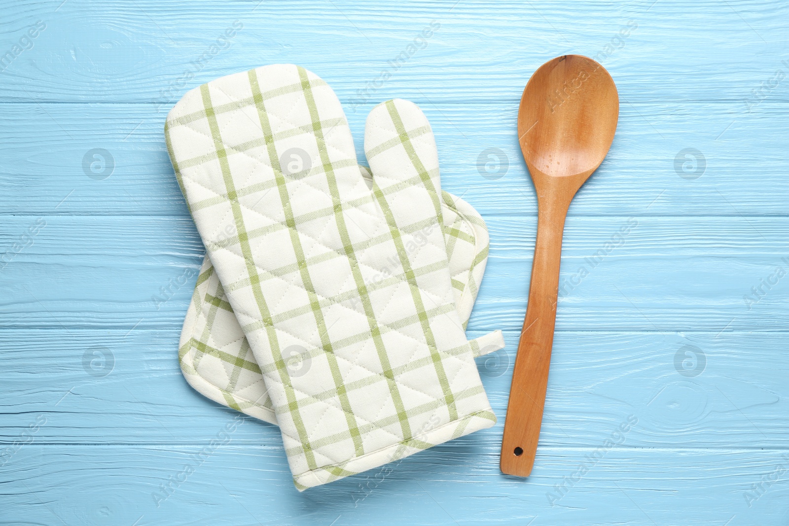 Oven glove, potholder and spoon on light blue wooden background, flat lay Photo of Oven glove, potholder and spoon on light blue wooden background, flat lay