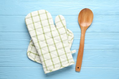 Photo of Oven glove, potholder and spoon on light blue wooden background, flat lay