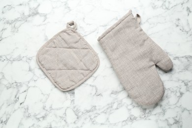 Photo of Oven glove and potholder on white marble table, flat lay