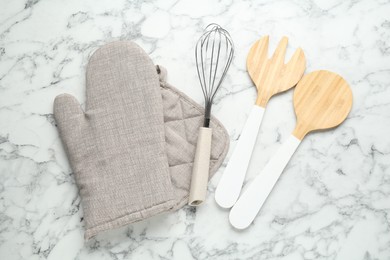 Photo of Oven glove, potholder and other kitchen utensils on white marble table, flat lay