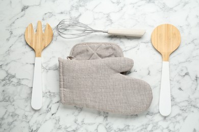 Photo of Oven glove, potholder and other kitchen utensils on white marble table, flat lay