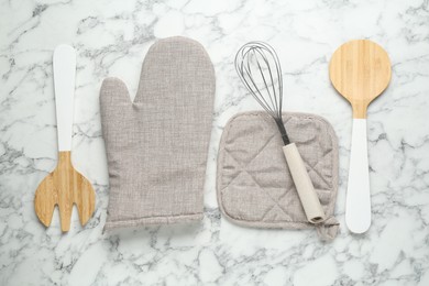 Photo of Oven glove, potholder and other kitchen utensils on white marble table, flat lay
