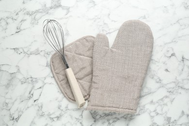 Photo of Oven glove, potholder and whisk on white marble table, flat lay