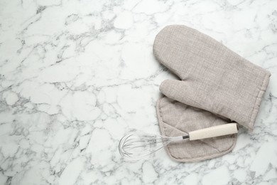 Photo of Oven glove, potholder and whisk on white marble table, flat lay. Space for text