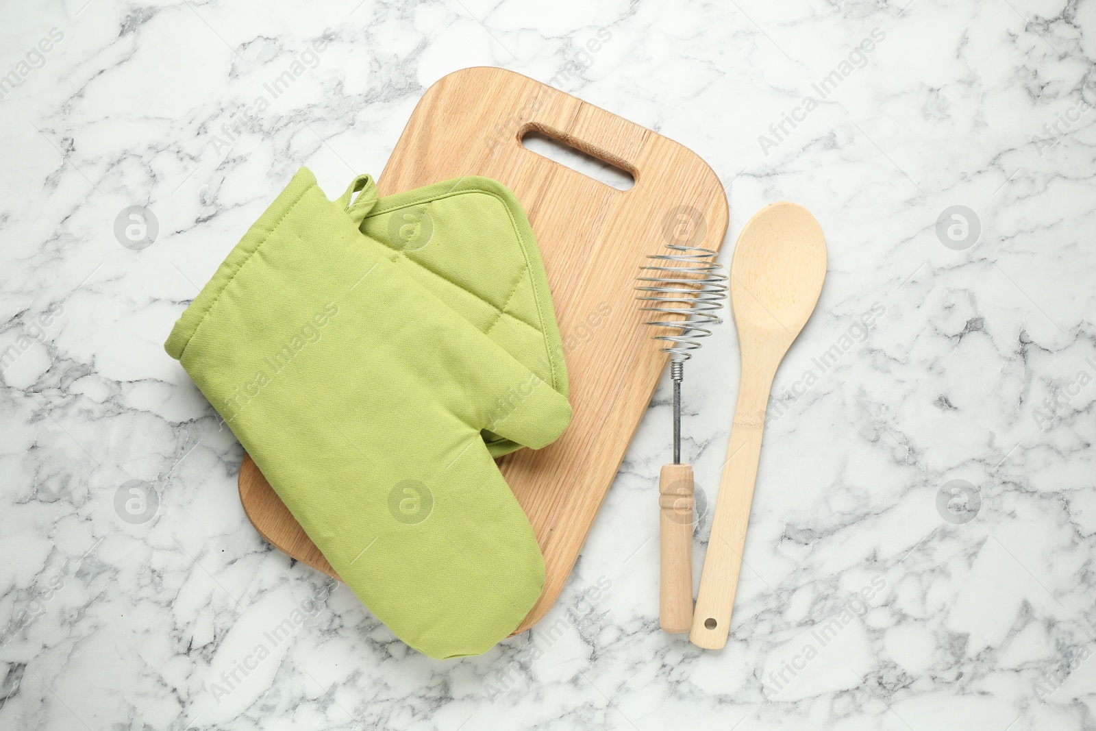 Photo of Oven glove, potholder and other kitchen utensils on white marble table, flat lay