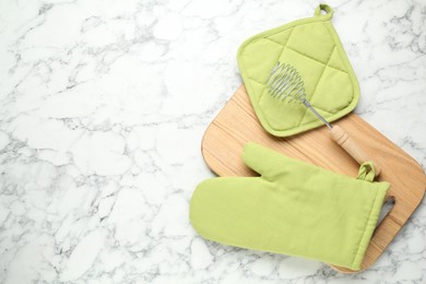 Photo of Oven glove, potholder and other kitchen utensils on white marble table, flat lay. Space for text