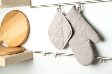 Photo of Oven glove and potholder hanging on metal rack in kitchen