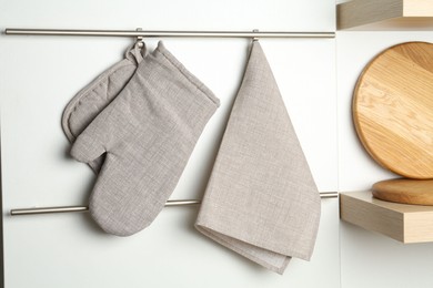 Photo of Oven glove, potholder and towel hanging on metal rack in kitchen