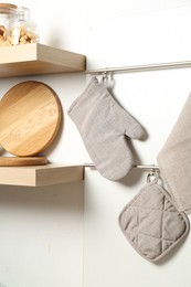 Photo of Oven glove, potholder and towel hanging on metal rack in kitchen