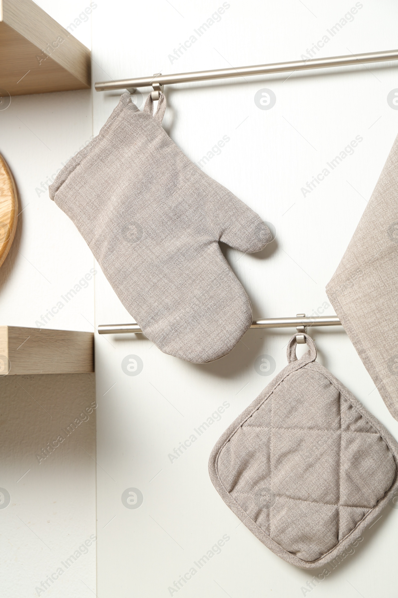 Photo of Oven glove, potholder and towel hanging on metal rack in kitchen