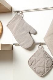 Photo of Oven glove, potholder and towel hanging on metal rack in kitchen