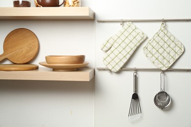 Photo of Oven glove, potholder and other kitchen utensils on metal rack indoors