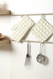 Photo of Oven glove, potholder and other kitchen utensils on metal rack indoors