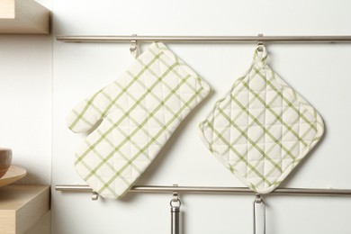 Photo of Oven glove and potholder hanging on metal rack in kitchen