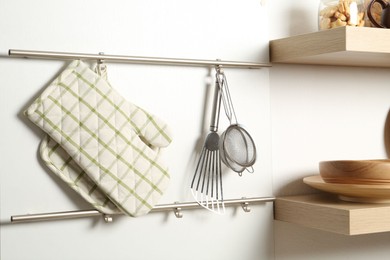 Photo of Oven glove, potholder and other kitchen utensils on metal rack indoors