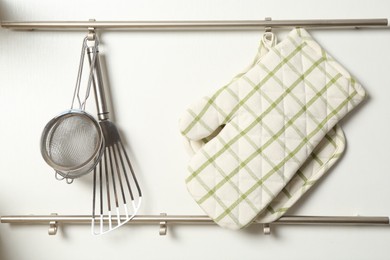Photo of Oven glove, potholder and other kitchen utensils on metal rack indoors