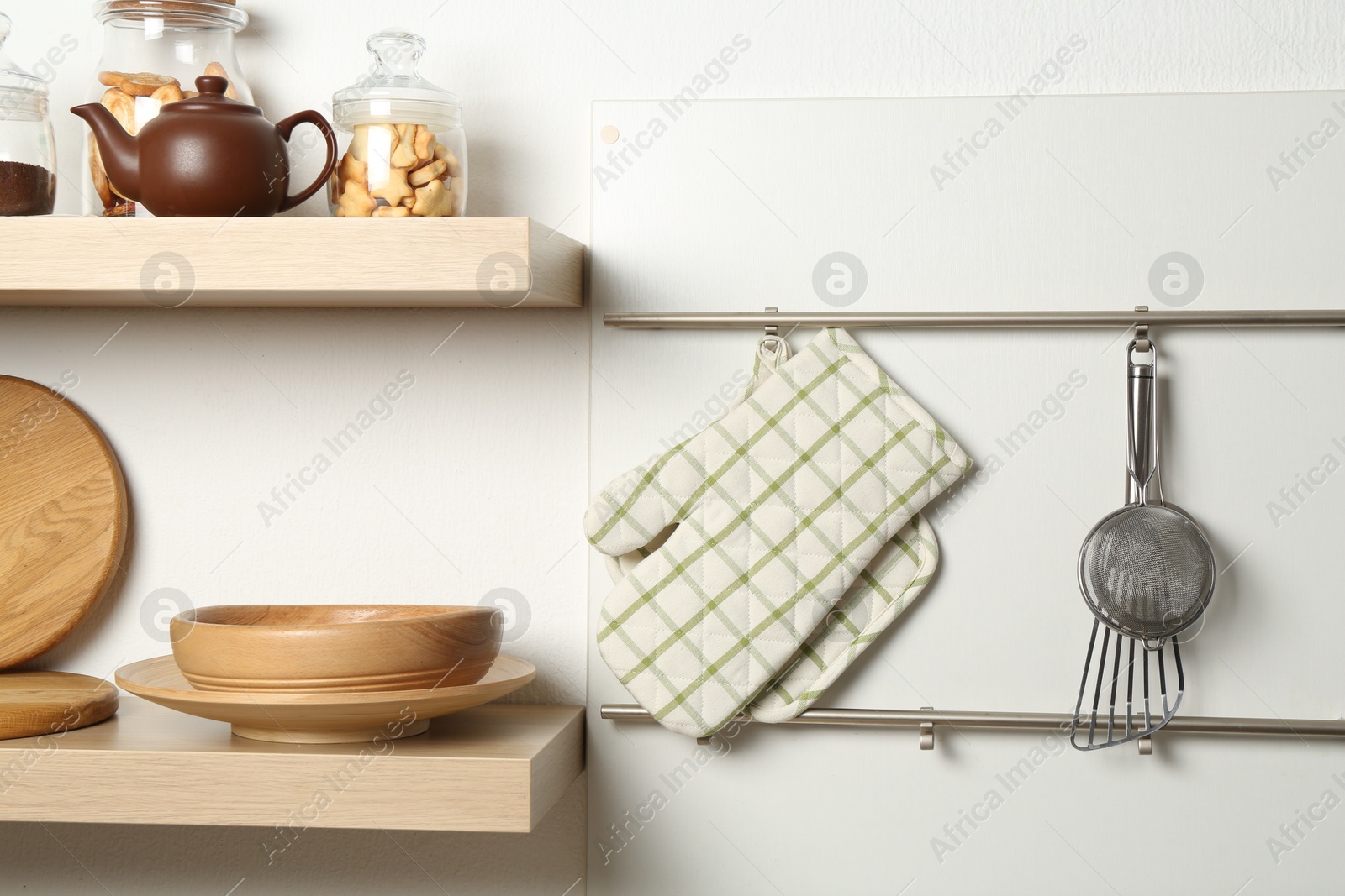 Photo of Oven glove, potholder and other kitchen utensils on metal rack indoors