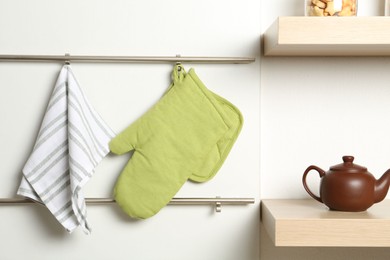 Photo of Oven glove, potholder and towel hanging on metal rack in kitchen
