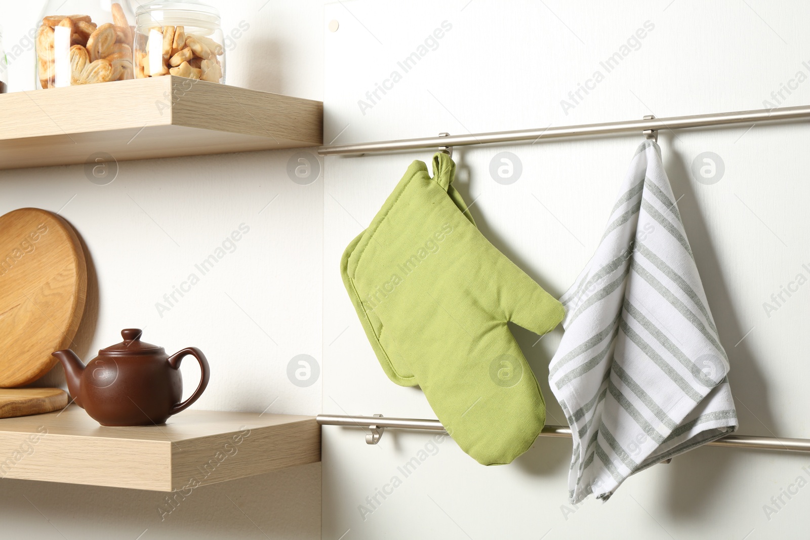 Photo of Oven glove, potholder and towel hanging on metal rack in kitchen