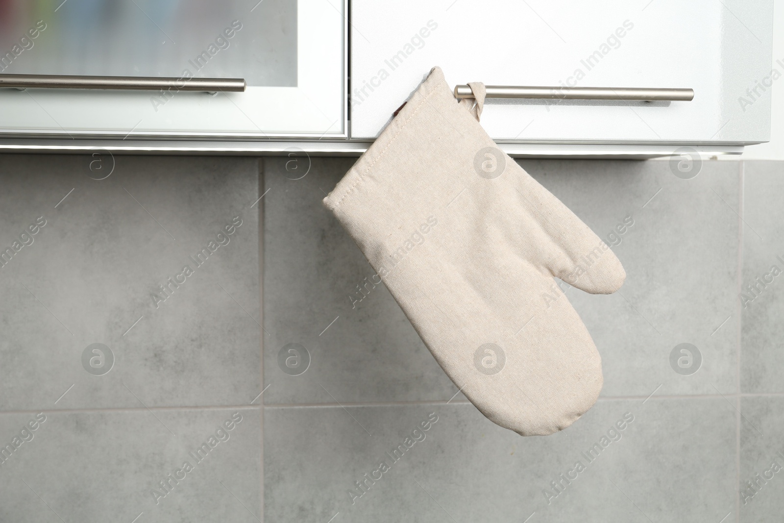 Photo of Oven glove hanging on handle of cabinet in kitchen
