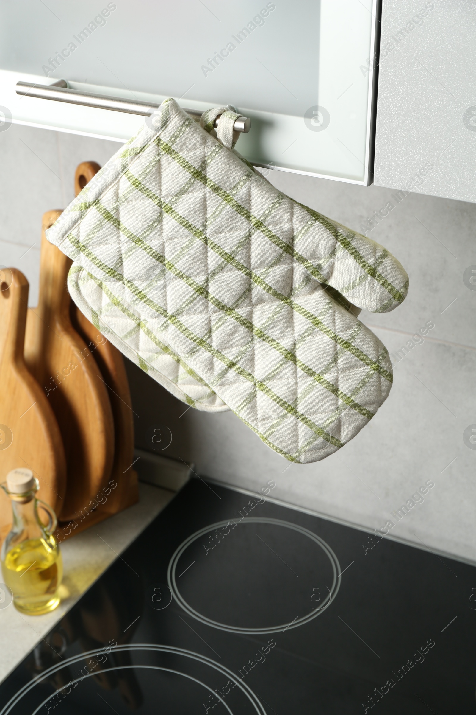Photo of Oven glove and potholder hanging on handle of cabinet in kitchen