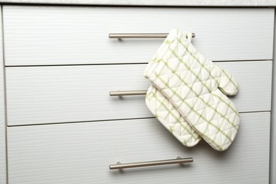 Photo of Oven glove and potholder hanging on handle of cabinet in kitchen