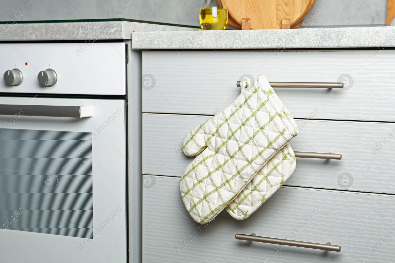 Oven glove and potholder hanging on handle of cabinet in kitchen Photo of Oven glove and potholder hanging on handle of cabinet in kitchen