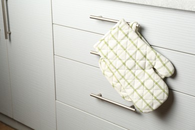 Photo of Oven glove and potholder hanging on handle of cabinet in kitchen