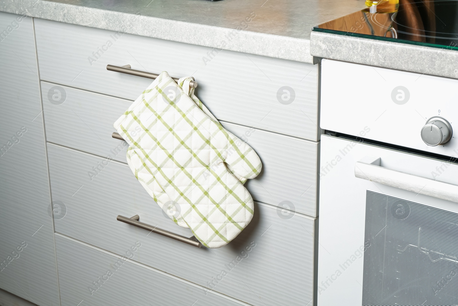 Oven glove and potholder hanging on handle of cabinet in kitchen Photo of Oven glove and potholder hanging on handle of cabinet in kitchen