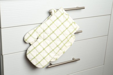 Photo of Oven glove and potholder hanging on handle of cabinet in kitchen