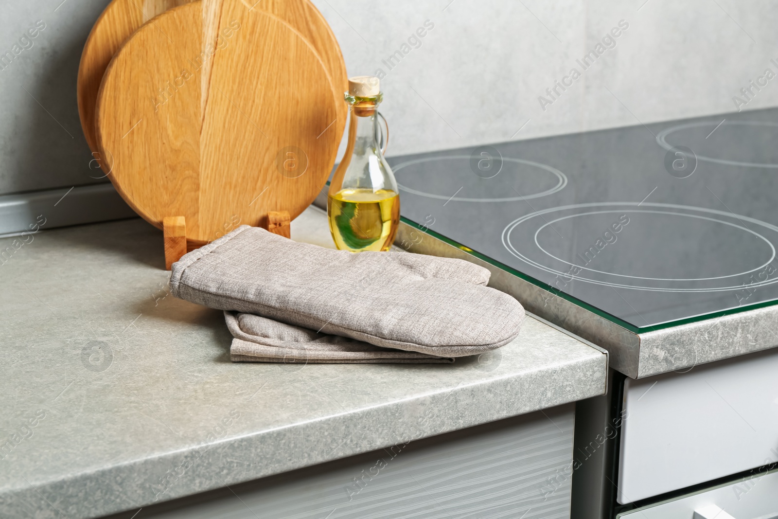 Oven glove, potholder, cutting boards and oil on grey countertop in kitchen Photo of Oven glove, potholder, cutting boards and oil on grey countertop in kitchen